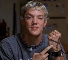 a young man with glasses and piercings on his fingers pointing to the cross in front of him