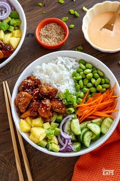 two bowls filled with rice, meat and veggies next to chopsticks