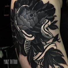 a black and white flower tattoo on the right side of the arm, with a snake crawling through it