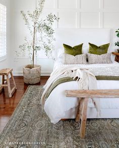 a bed with pillows and blankets on top of it next to a wooden bench in front of a window