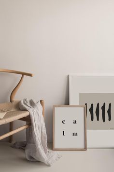 a wooden chair next to a white wall with a black and white print on it