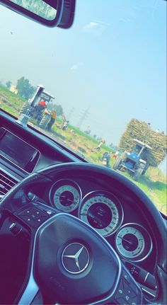 the steering wheel and dashboard of a car on a country road with trucks in the background