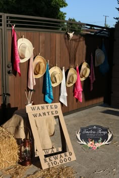 several hats are hanging on a fence near a sign that reads wanted wanted reward $ 1, 000