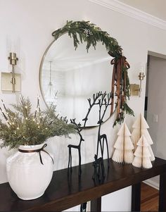 a mirror sitting on top of a wooden table next to a white vase filled with greenery