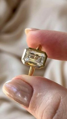 a close up of a person's hand holding a ring with an emerald stone