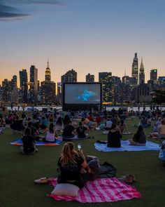 many people are sitting on the grass watching movies in front of a cityscape