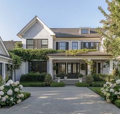 a large white house with lots of windows and bushes in front of it, along with flowers on either side of the door