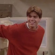 a young man standing in front of an open refrigerator freezer smiling at the camera