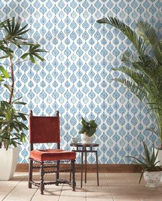 a chair and table in front of a wallpapered room with potted plants