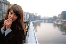 a woman standing on the side of a river next to buildings and looking off into the distance