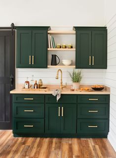 a kitchen with dark green cabinets and wooden floors is pictured in this image, there are shelves on the wall above the sink