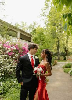 a man and woman standing next to each other in front of some bushes with flowers