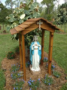 a statue of the virgin mary under a wooden gazebo with blue flowers around it