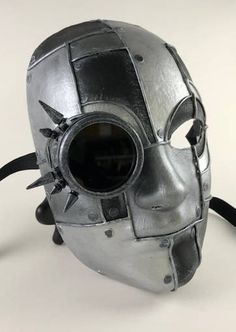 "A futuristic, (or post-apocalyptic), masquerade full face mask. This mask if handmade from paper mache and also incorporates real metal spikes and a real glass lens. Hand painted and designed to look like riveted sheets of distressed metal or iron. You can see through the tinted glass lens - just like heavily tinted sunglasses. The mask has traditional black ribbon ties for a comfortable fit. The mask's dimensions are approximately 7\" wide, 9\" high and 3 ½\" deep." Alternative Fashion Masks For Cosplay Events, Punk Full Face Masks For Costume Party, Futuristic Masks And Prosthetics For Halloween Costume Party, Futuristic Masks And Prosthetics For Halloween Masquerade, Steampunk Mask For Costume Party, Fantasy Full Face Mask For Cosplay Events, Futuristic Masks For Masquerade And Cosplay Events, Futuristic Masks And Prosthetics For Halloween, Cyberpunk Masks And Prosthetics For Masquerade And Cosplay