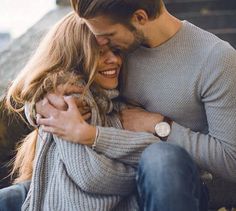 a man and woman hugging each other while sitting on the ground with their arms around each other