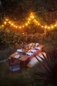 an outdoor dining table with lights strung over it