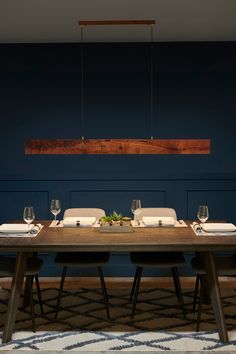 a wooden table with place settings and wine glasses on it in front of a blue wall