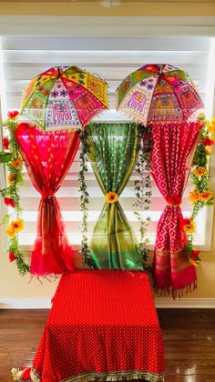 three colorful umbrellas hanging from the side of a window in front of a red table cloth