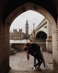 two people are standing in an archway looking at the water and big ben clock tower