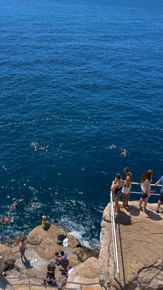 people are swimming in the ocean near some rocks and stairs with steps leading up to them