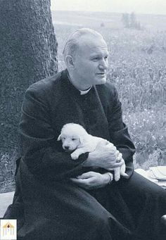 an older man holding a small white puppy in his lap while sitting next to a tree