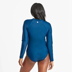 a woman in a blue bodysuit with her back turned to the camera, looking down