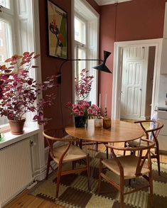 a dining room table and chairs in front of a window with potted plants on it