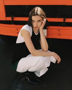 a woman sitting on the ground next to an orange truck with her hand under her head