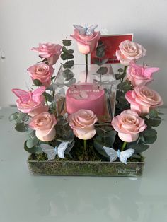 pink roses are arranged in a clear vase with moss and butterflies on the table next to it