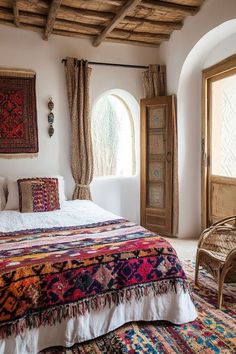 a large bed sitting under a window next to a chair and rug on top of a floor