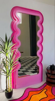 a pink mirror sitting next to a potted plant on top of a white table