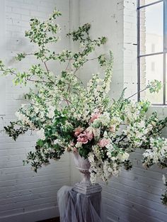 a vase filled with white and pink flowers on top of a wooden table next to a window