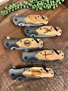 three knives are sitting on top of a wooden table next to some green leaves and flowers