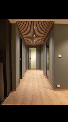 an empty hallway with wood flooring and lighting on either side of the corridor, leading to another room