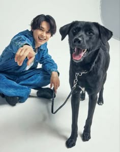 a man kneeling down next to a black dog on a white floor and pointing at the camera