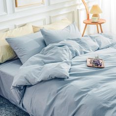 an unmade bed with blue sheets and pillows on the floor next to a lamp