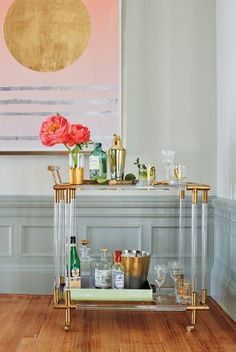 a bar cart with drinks on it in front of a painting and wooden flooring