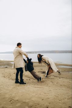 two people playing with each other on the beach near water and sand, while one person holds his leg up in the air