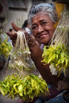 an old woman is holding some plants in her hands