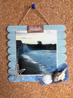 an ocean scene is hanging on the cork board with a starfish and seashell