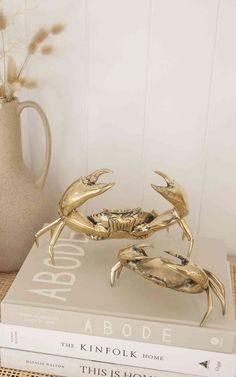 two gold crab figurines sitting on top of a book next to a vase