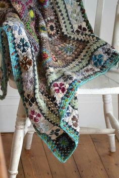 a crocheted blanket sitting on top of a white chair next to a wooden floor