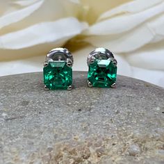 "The stud earrings pictured are lab created emerald #5519. Also shown in white gold. Earring back style is subject to change due to availability. -Approximate total carat weight: 2.00ctw. -Center Stone Size: 6x6mm - approx. 1.00ct each diamond equivalent -Center Stone Shape: Asscher cut -Gem Type: lab created emerald -Stone Clarity: VS2 -Stone Color: lively medium green, eye-clean -Moh's Scale: 8.5 hardness -Metal Type and Purity: 14k yellow gold -Setting: 4 prong basket head -Backing: friction Classic Green Earrings For Anniversary, Classic Emerald Earrings For Anniversary, Emerald Birthstone Earrings For Anniversary, May Birthstone Earrings For Anniversary, Classic Emerald Earrings For May Birthstone, Green Earrings For Anniversary, Classic May Birthstone Earrings As Gift, Classic Earrings For May Birthstone Gift, Classic Earrings As Gift For May Birthstone