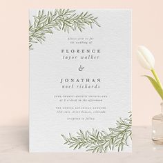 a white and green wedding card with greenery