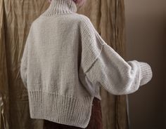 a woman in a white sweater and brown pants is looking at her reflection in the mirror