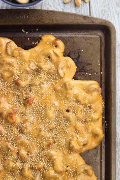 a pan filled with food on top of a wooden table next to a bowl of cashews