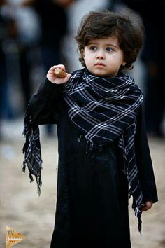 a young boy wearing a scarf and holding an apple in one hand while walking down the street