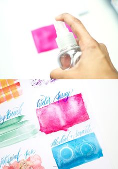 a hand holding a spray bottle over some watercolor paper with different colors on it