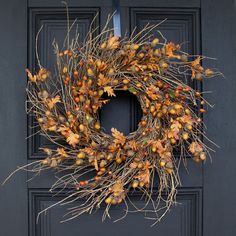 a wreath is hanging on the front door with autumn leaves and acorns around it