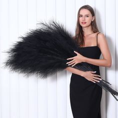 a woman in a black dress is holding a large feather fan and posing for the camera